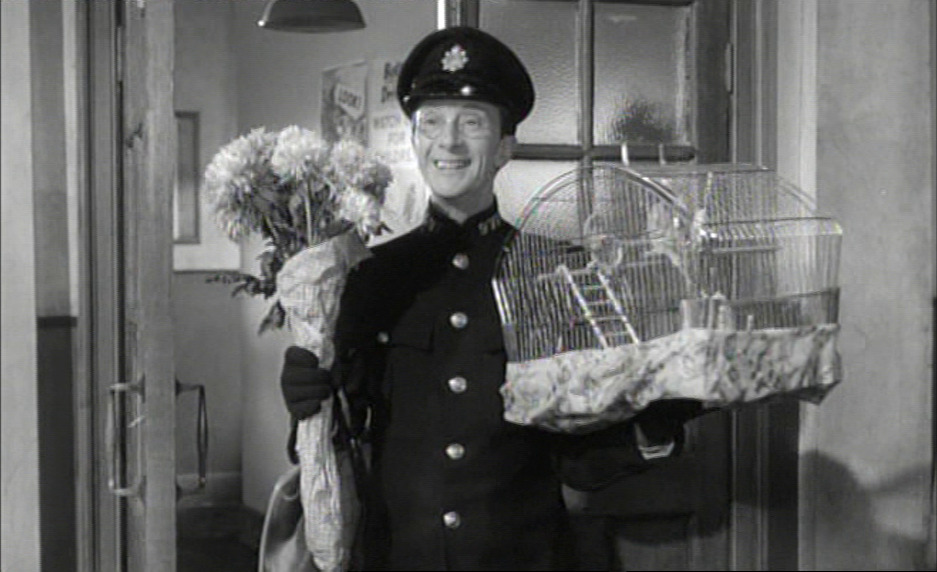 Charles Hawtrey as a policeman holding a bouquet of flowers.